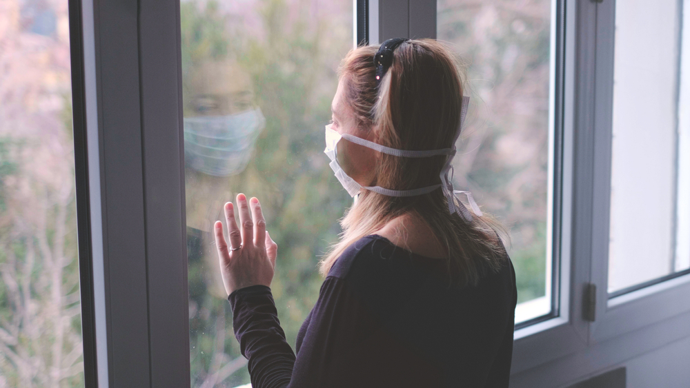 Woman staring out a window wearing a facemask